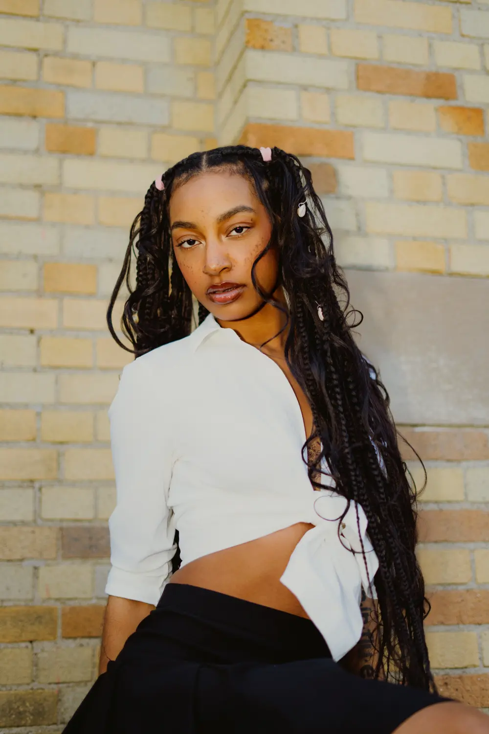 Close portrait of a woman with long braids in a white shirt against a brick wall