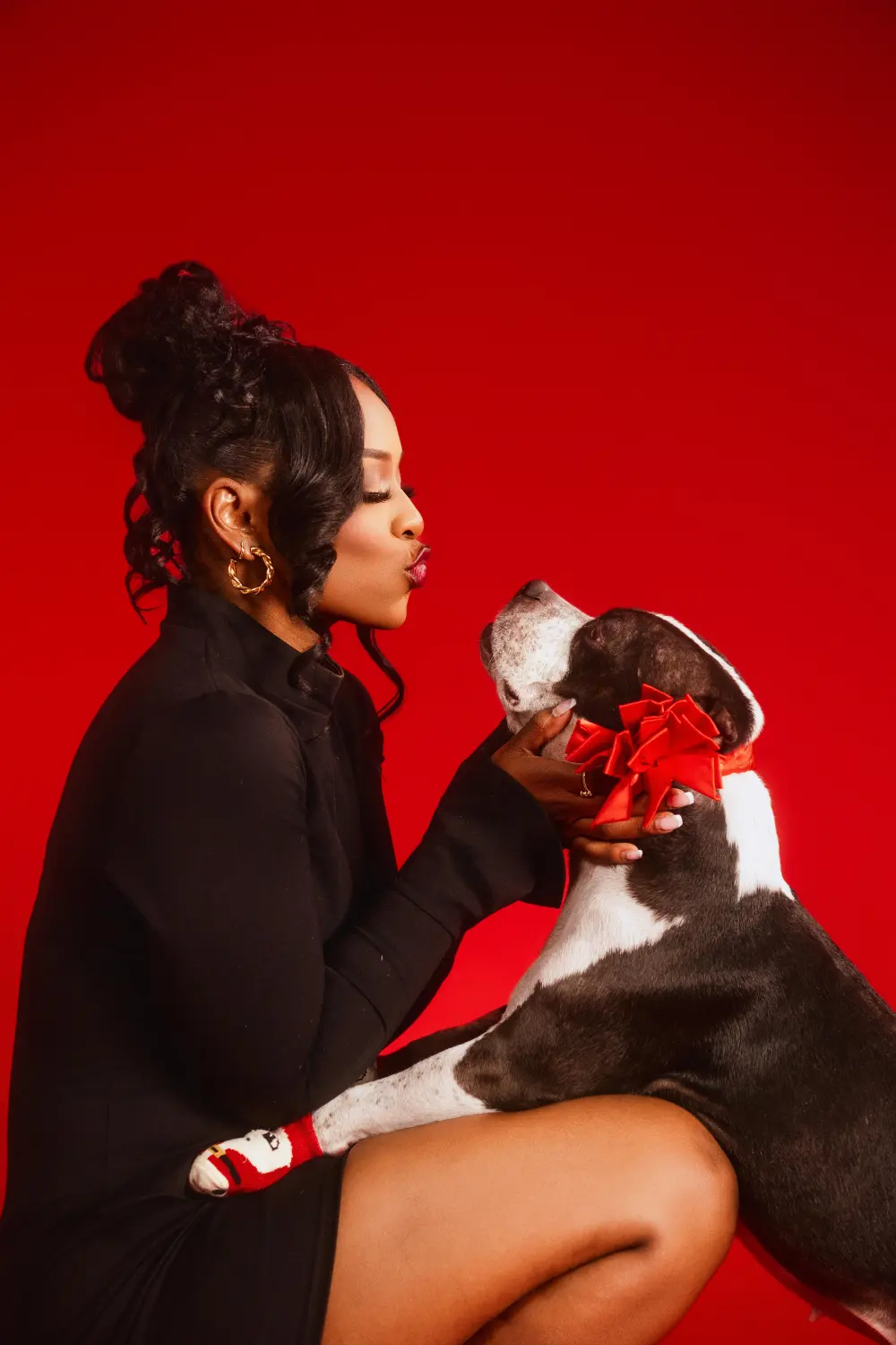 Woman in black holding a dog with a red bow against a red backdrop