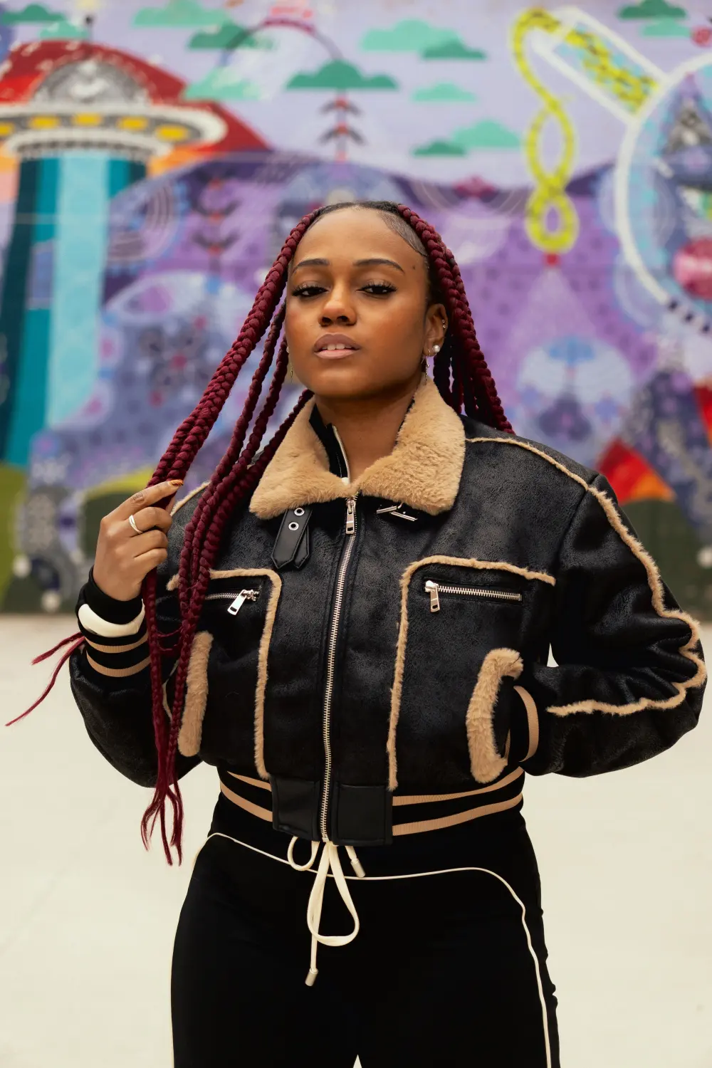 Woman with long red braids in a black and cream jacket in front of a colorful mural